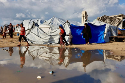 Displaced Palestinians walk past a large pool of standing water in Gaza City. Heavy winter rains have have made an already precarious life worse for displaced Gazans - Omar AL-QATTAA (AFP)