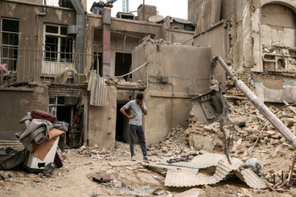 A man speaks on a mobile phone as he stands outside damaged homes, following a military strike on the Iranian capital Tehran on March 15, 2026. - Atta KENARE (AFP)