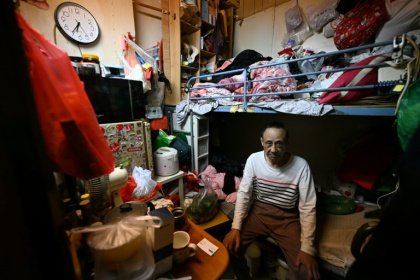 Guan Ci sits on his bed in his subdivided housing unit in Kowloon, Hong Kong - Peter PARKS (AFP)